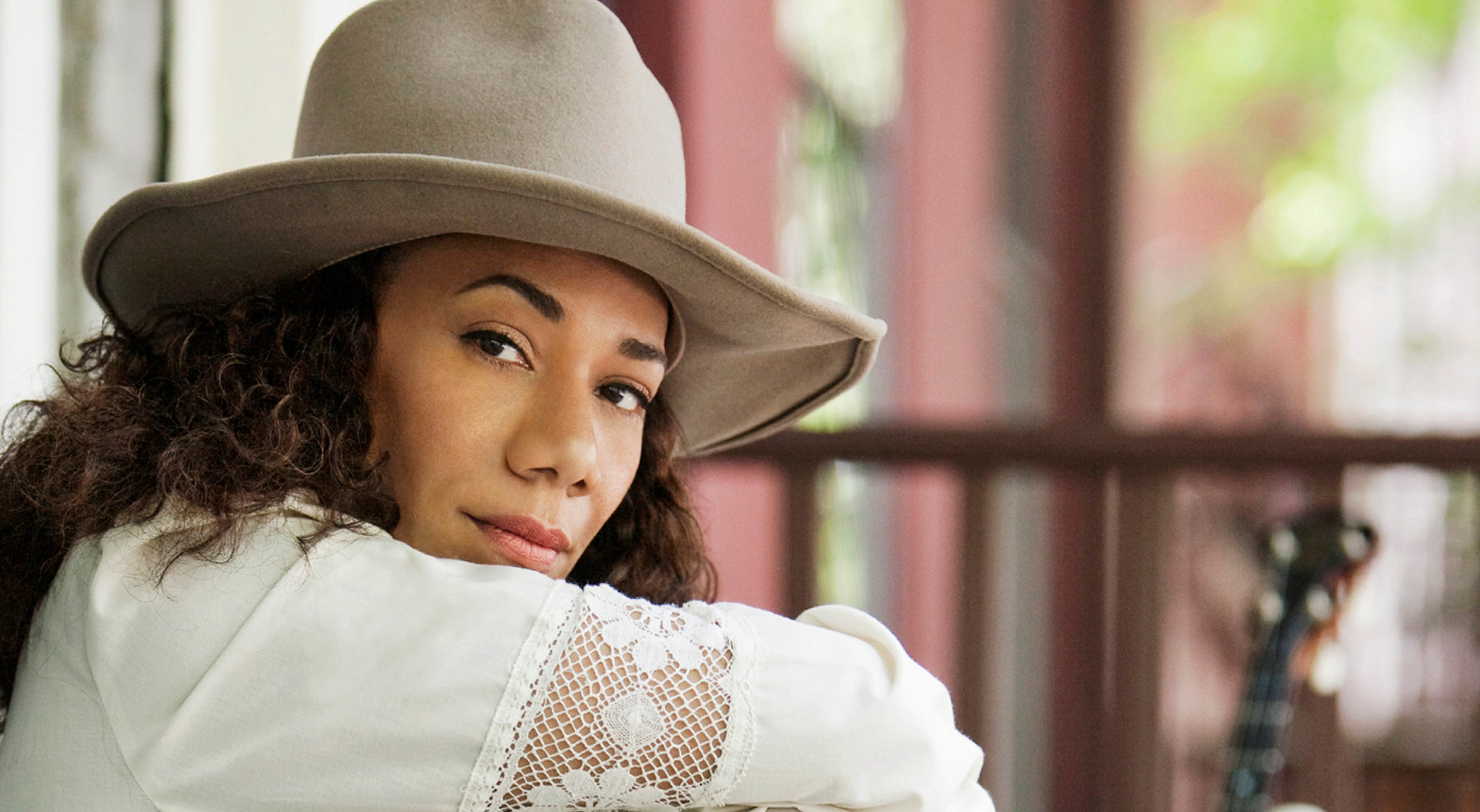 A close up portrait of Martha Redbone. She is wearing a white dress with long sleeves and a greyish tan rimmed hat. 